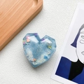 Detail of blue heart resin phone socket with glitter, sequins, and pearl on white surface - Blue
