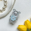 Detail eines Bärengriffes mit Glitzerfüllung und blauer Blume auf weißer Oberfläche - Blau