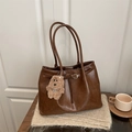 Deep brown vintage tote bag with belt detail and plush puppy charm on knitted background - Brown