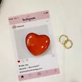 Glänzender roter Herz-Handygriff mit goldenen Hohlringen auf einer Displaykarte - Dunkelorange