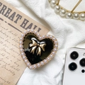 Dettaglio del supporto per telefono a cuore con fiocco dorato e perle su sfondo vintage - Fiocco a Cuore in Metallo - Nero / Nero