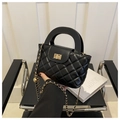 Schwarze gesteppte Handtasche mit goldener Kette und Kugelanhänger auf Designstuhl - Schwarz