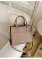 Dettaglio borsa tote in pelle PU tortora con borchie metalliche e logo su un divano - Cachi