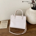 Elegant beige leather tote bag with top handles on a minimalist wooden table setting - White