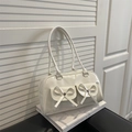 Glossy white underarm bag with decorative bows and front pockets on a book - White