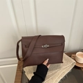 Bolso de mano marrón oscuro con cierre plateado sobre una mesa de madera clásica - Marrón