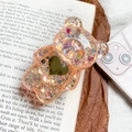 Dettaglio del supporto per telefono orso 3D con glitter su sfondo di libro aperto - Arancione