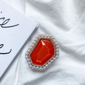 Macro shot of red gemstone phone grip with pearl and rhinestone inlay on white fabric - Orange