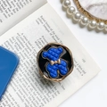 Soporte para móvil de oso azul acolchado con lazo dorado sobre fondo de libro viejo - Oso Azul Real - Base Negra