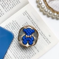 Soporte de móvil de oso azul con lazo dorado y textura de diamante sobre un libro - Oso Azul Real - Base Blanca