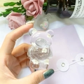 Detail of transparent bear phone grip with embedded white dried flowers held in hand - White
