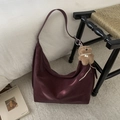 Dettaglio borsa hobo in pelle bordeaux scuro con ciondolo a orsetto su tappeto bianco - Con Ciondolo / Rosso