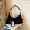 Black leather dumpling crossbody bag with braided rope detail on a white book - Black