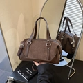Bolso Boston retro de ante marrón oscuro con herrajes plateados y asas sobre una mesa negra - Marrón
