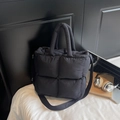Large black quilted puffer tote bag with handles and strap on a white bed - Black