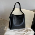 Minimalist black leather bucket tote bag with adjustable strap on a chair - Black