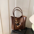 Grand sac cabas en cuir marron avec breloque lapin sur des livres devant un mur blanc - Avec Pendentif / Marron