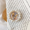 Detailed close-up of a golden bow phone grip with sparkling rhinestones and white pearls - Strapped Bow / White