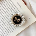 Detail view of a vintage round pop socket with a gold bow, rhinestones, and pearls - Dotted Line Bow / Black