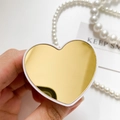 Nahaufnahme der herzförmigen Handyhalterung mit Goldspiegel in der Hand mit Schmuck - Herz / Herz Gold Weiß