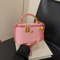 Rosa Box-Handtasche mit goldener Rundgriff und gewebtem Kettenriemen in der Hand - Rosa