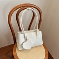 Bolso de hombro crema con un colgante de monedero de corazón sobre una silla de mimbre - Blanco