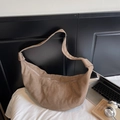 Grand sac croissant en daim marron avec bandoulière à nœud plissé sur literie blanche - café