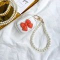 Detail of transparent AirPods case featuring a 3D red bow and white faux pearl wrist strap - Orange / AirPods 1/2