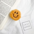 Close-up of yellow plush smiley face mobile phone stand on soft white linen fabric - Yellow