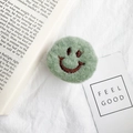 Close-up of a green plush smiley face phone socket on white fabric with an English book - Green