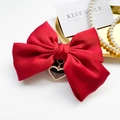 Detail of red satin bow phone grip with heart pearl charm on a minimalist white display - Red