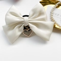 Close-up of a white satin bow phone grip with a pearl heart pendant and golden frame - White