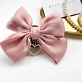 Detail of pink satin bow phone grip featuring a hollow heart pearl pendant on white desk - Pink