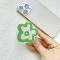 Close-up of a green flower-shaped acrylic phone grip with a white folding base on a phone - Green Flower