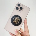 Handheld shot of round black resin MagSafe grip with gold foil flakes on a phone - Magnetic Stand / Light Rose Gold Foil (Black Base)