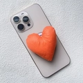 Detail of a bright orange heart-shaped padded fabric magnetic phone stand on a grey phone - Magnetic Stand / Orange Fabric Heart