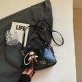 Bolso cubo de cuero negro con colgante y cadena de perlas sobre un traje gris suave - Con Colgante / Negro
