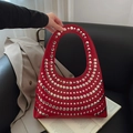 Red glossy leather handbag with silver rivets and oval handle in lifestyle setting - Red