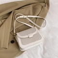 Beige Umhängetasche mit gewebter Klappe und goldener Schnalle auf Blazer-Hintergrund - Weiß