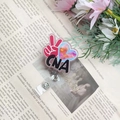 Detail of retractable CNA badge reel with glossy decorative disk and clear PVC strap - Pink CNA Badge Reel