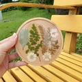 Posavasos de madera con flores secas reales y resina sostenido a mano en un jardín - Redondo No.2-13cm