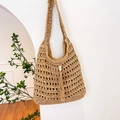 Bolso tote de paja marrón claro con borla y perla colgado en una pared blanca - Caqui