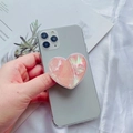 Detalle del soporte para móvil de corazón rosa perlado en smartphone gris con revistas - Vieira Rosa Con Borde Blanco