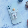 3D cartoon astronaut expanding phone grip on white smartphone with planet decor - Astronaut
