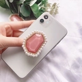 Pink gemstone phone grip with pearl and diamond accents held against a white fabric background - Pink with Pearl Border