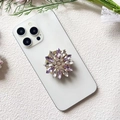Detailed view of luxury flower phone grip with purple and clear rhinestones on white phone - Gold Base Purple Marquise (Small Purple Diamond - Airbag Stand)