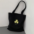Detailed close-up of lucky clover embroidery on black canvas tote bag surface - Black