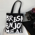 Dettaglio di una borsa tote in tela nera con testo artistico su una sedia minimalista - Nero
