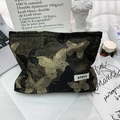 Dettaglio di un beauty case grande con ricamo a farfalla dorata e logo sulla scrivania - Borsa da Trucco Farfalla Dorata