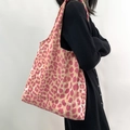 Grand sac fourre-tout à motif léopard rose et beige porté à l'épaule sur robe noire - Léopard Grand Rose